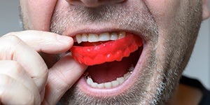 close up of a man putting a red mouthguard into his mouth 