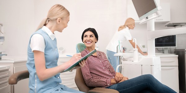 Woman smiling while dental assistant takes notes on clipboard