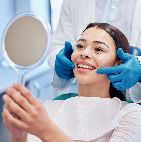 Woman smiling at reflection in handheld mirror