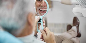 Older man smiling into a dental mirror