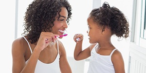 mother and young daughter brushing their teeth together 