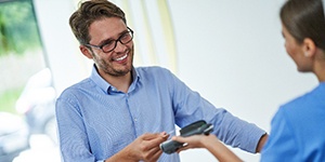 Man smiling while using credit card to pay for dental care