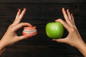 Person holding a pair of dentures and an apple in their hands